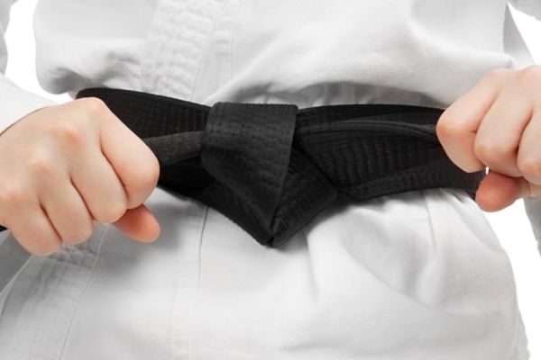 Judo-Anzug mit schwarzen Gürtel der mit Händen an den Schlaufen festgezogen wird